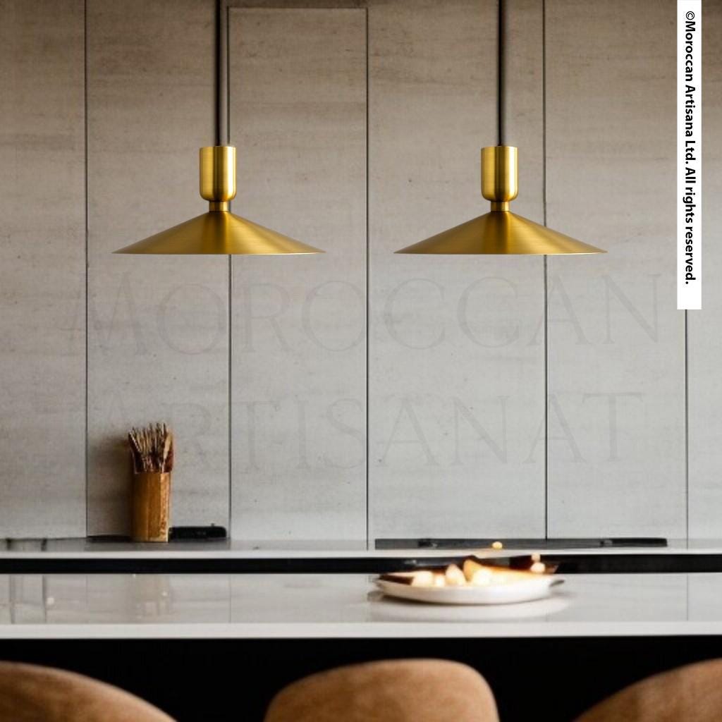 a modern dining area with a white table and two gold pendant lights hanging above it. There is a bowl of fruit on the table, and a vase is visible on the left side.