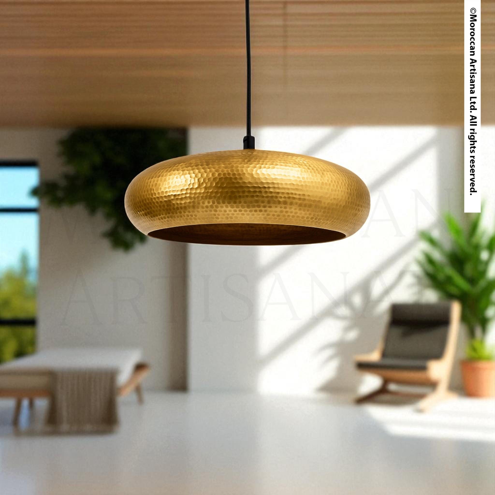 a modern, minimalist interior design with a large, round, gold-colored pendant light hanging from the ceiling. The room has a white ceiling and a wooden floor, creating a clean and elegant atmosphere. There is a chair and a potted plant in the background, adding a touch of greenery to the space.