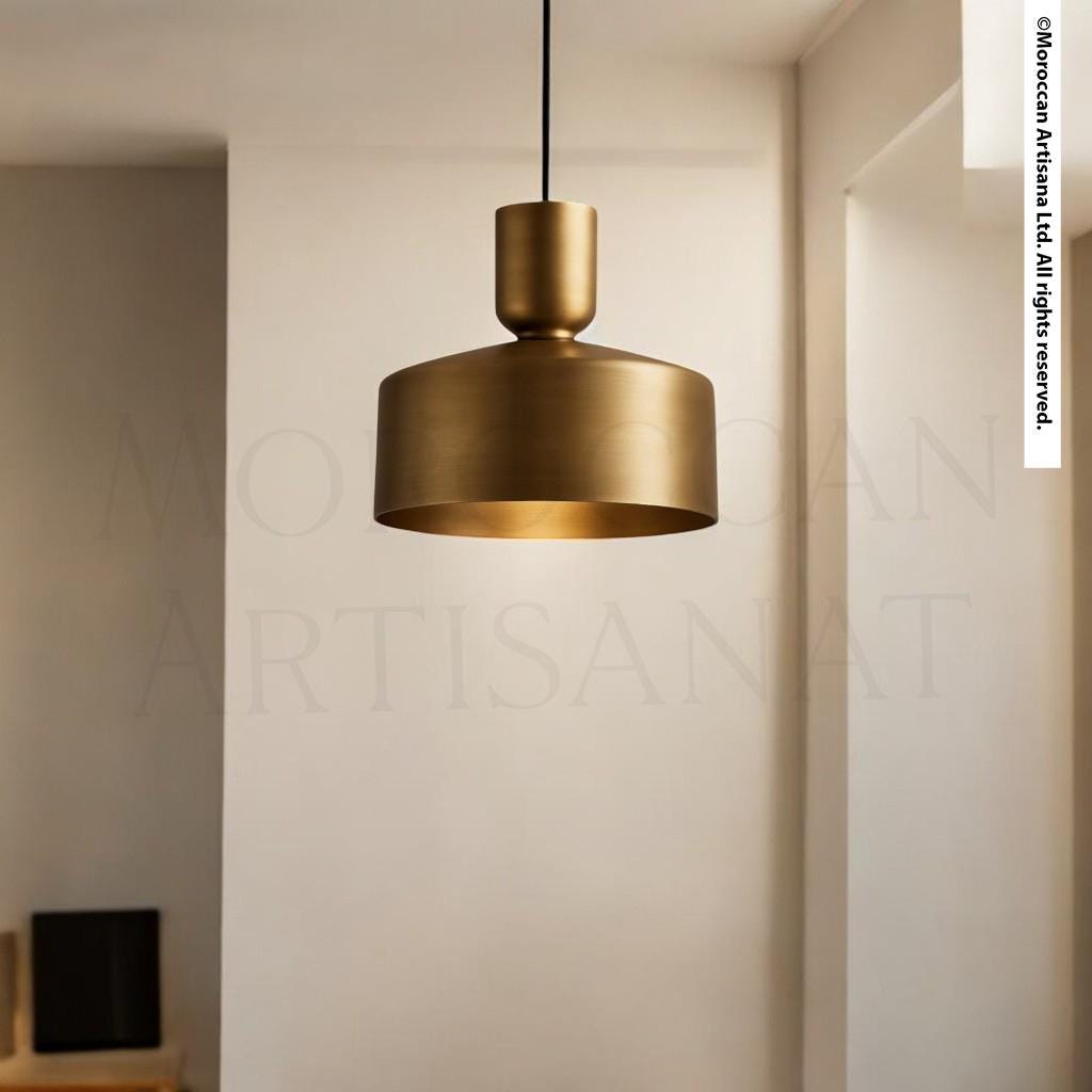 A modern gold-colored pendant light hangs from the ceiling in a minimalist room with white walls.