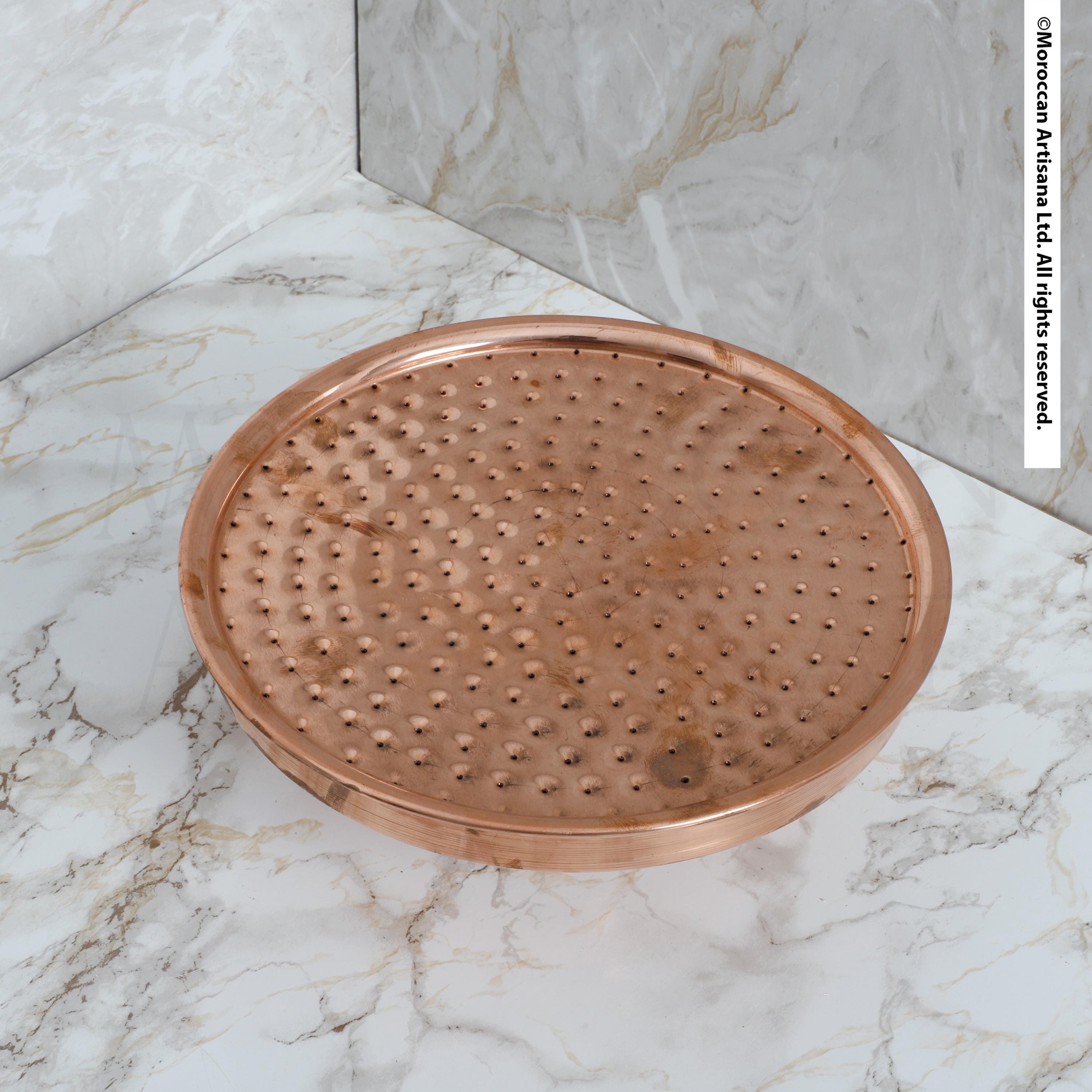 A copper-colored metal shower tray with a textured surface sits on a marble countertop.