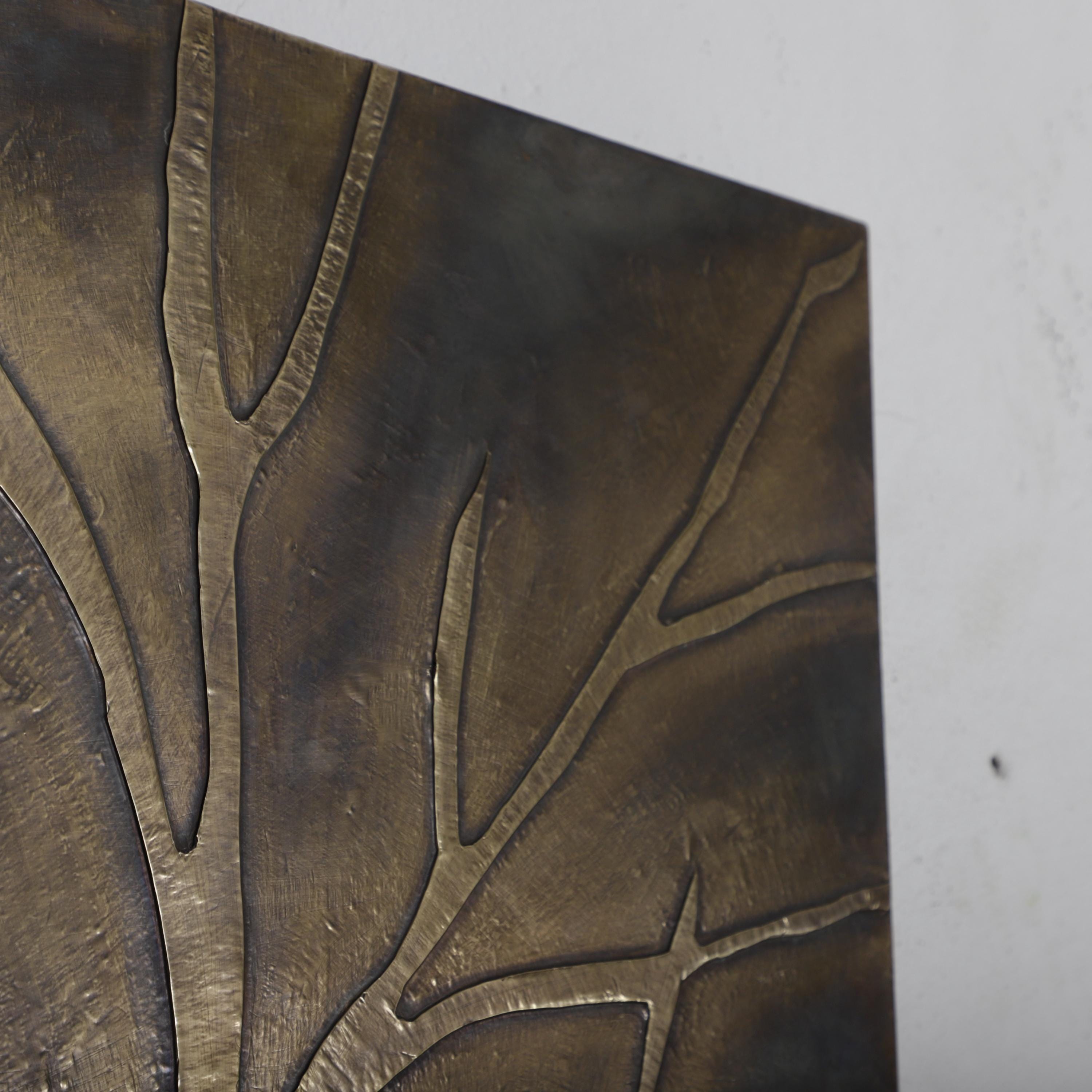 a close-up view of a textured surface, possibly a piece of metal or a painting, with a pattern of lines or branches. The surface appears to be dark in color, possibly bronze or brass, and has a rough, textured appearance.