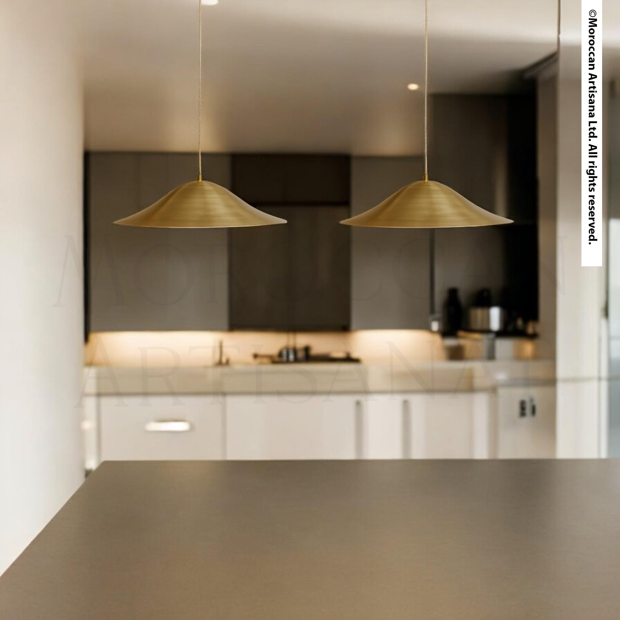 a modern kitchen with a sleek, minimalist design. Two pendant lights hang above a countertop, casting a warm glow over the space. The kitchen is equipped with white cabinets and a sleek, black countertop.