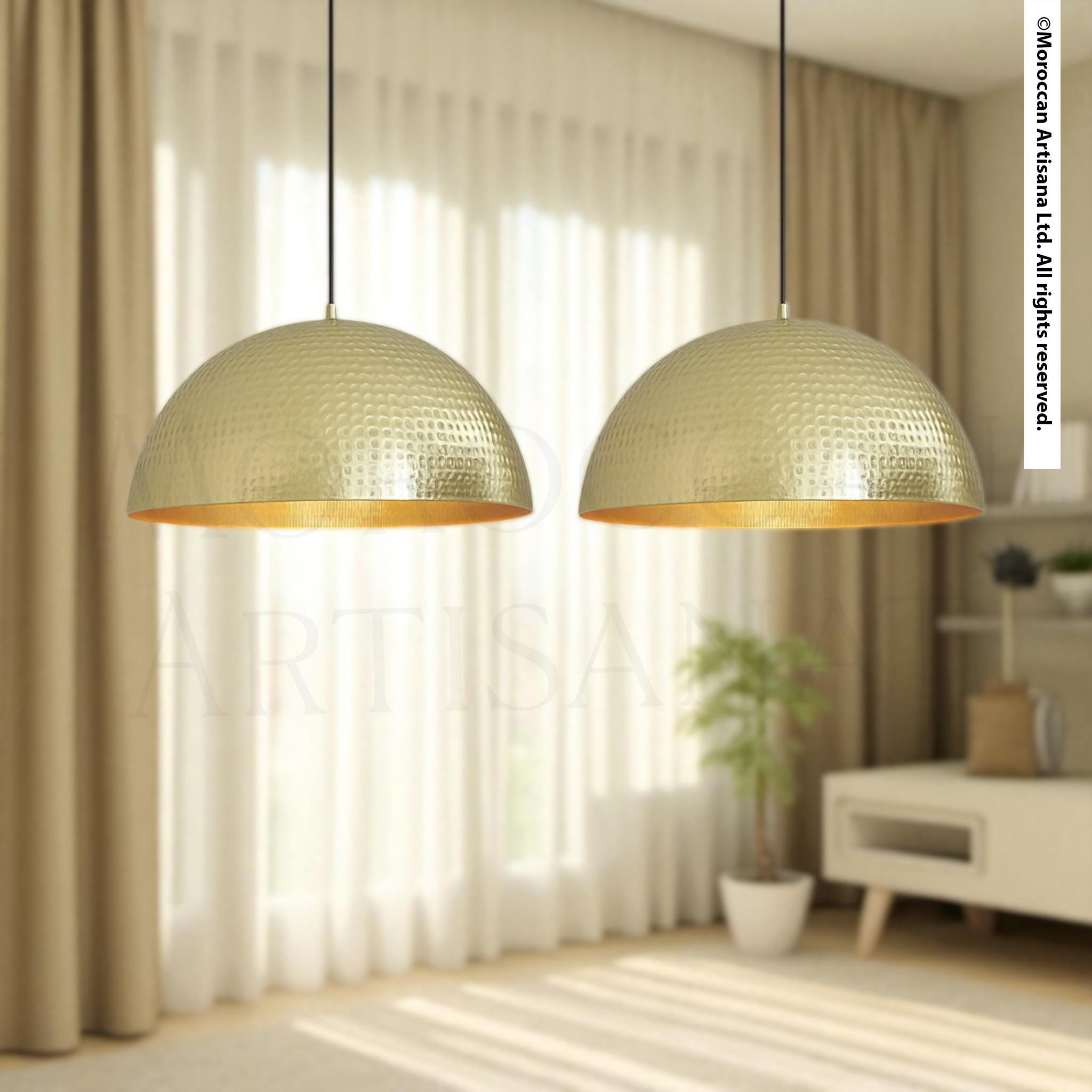 two gold-colored pendant lights hanging from the ceiling in a room with a window and a plant.