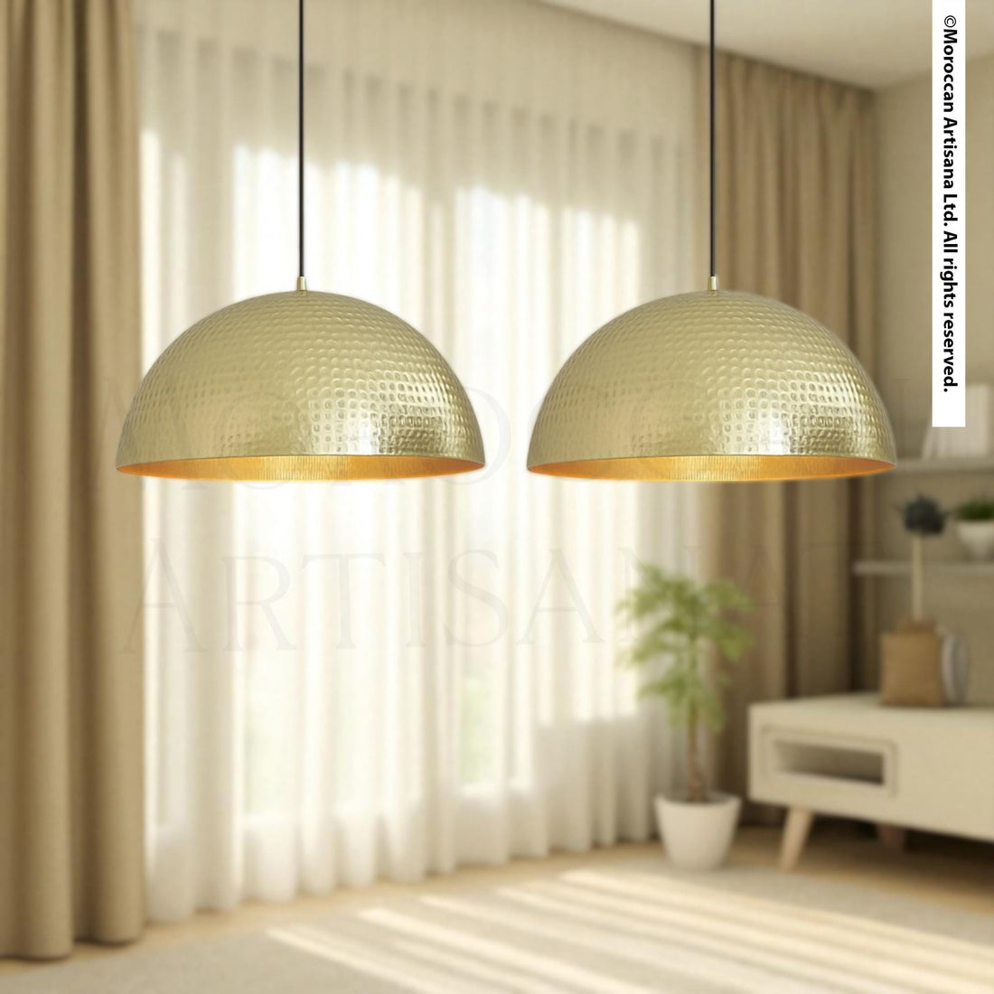 two gold-colored pendant lights hanging from the ceiling in a room with a window and a plant.