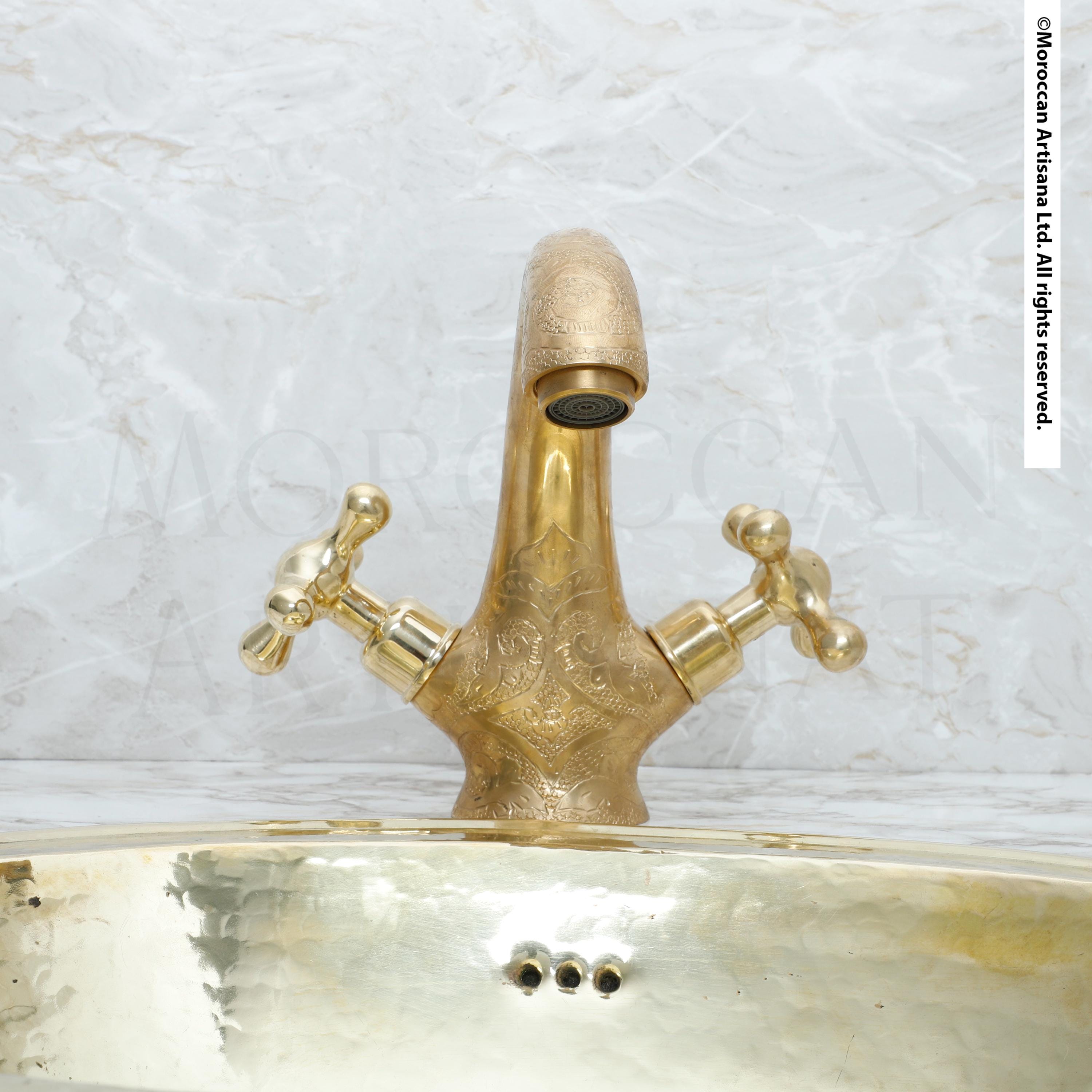 A gold-colored bathroom faucet with ornate decorations is shown against a marble background.