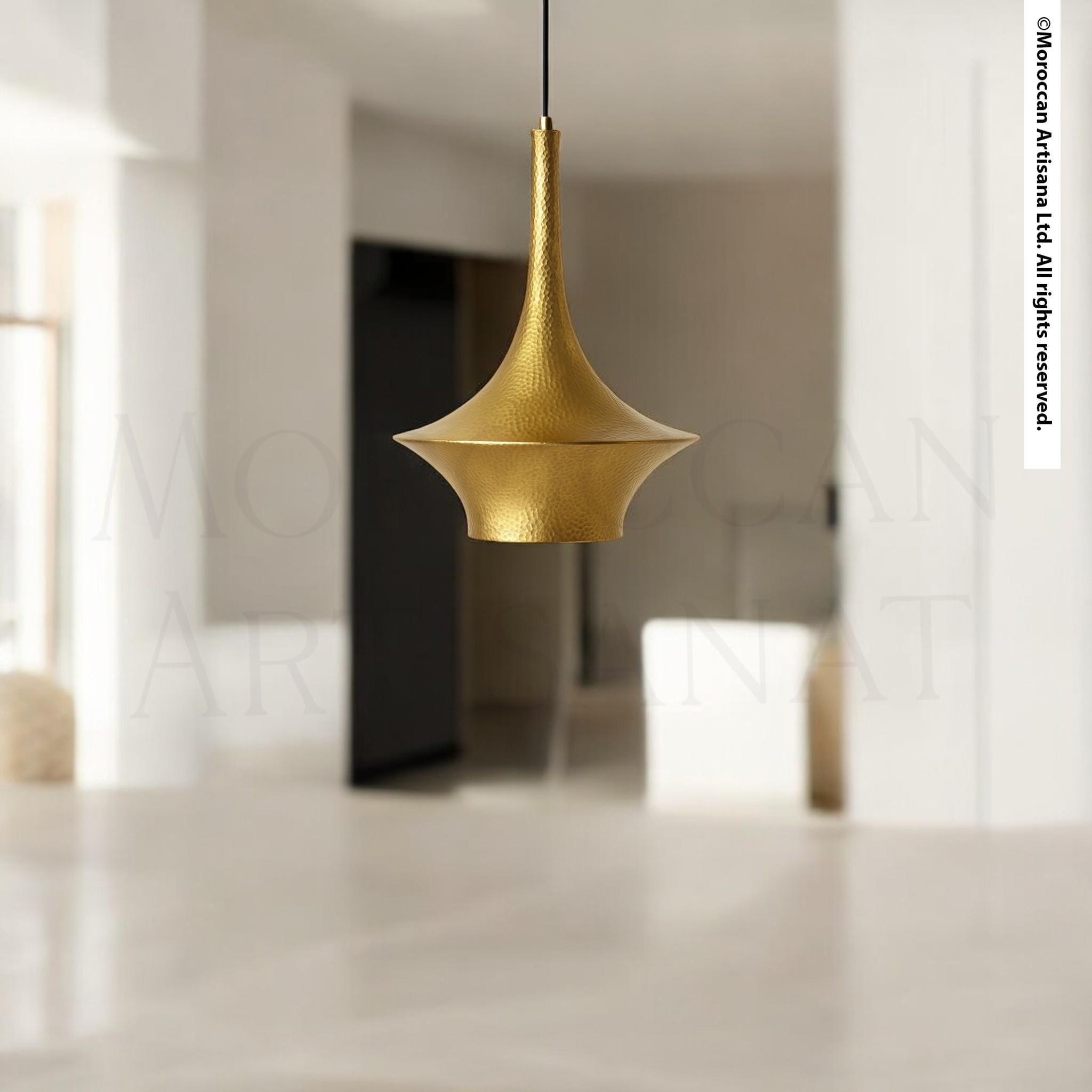 A gold-colored pendant light hangs from the ceiling in a minimalist, white-walled room.