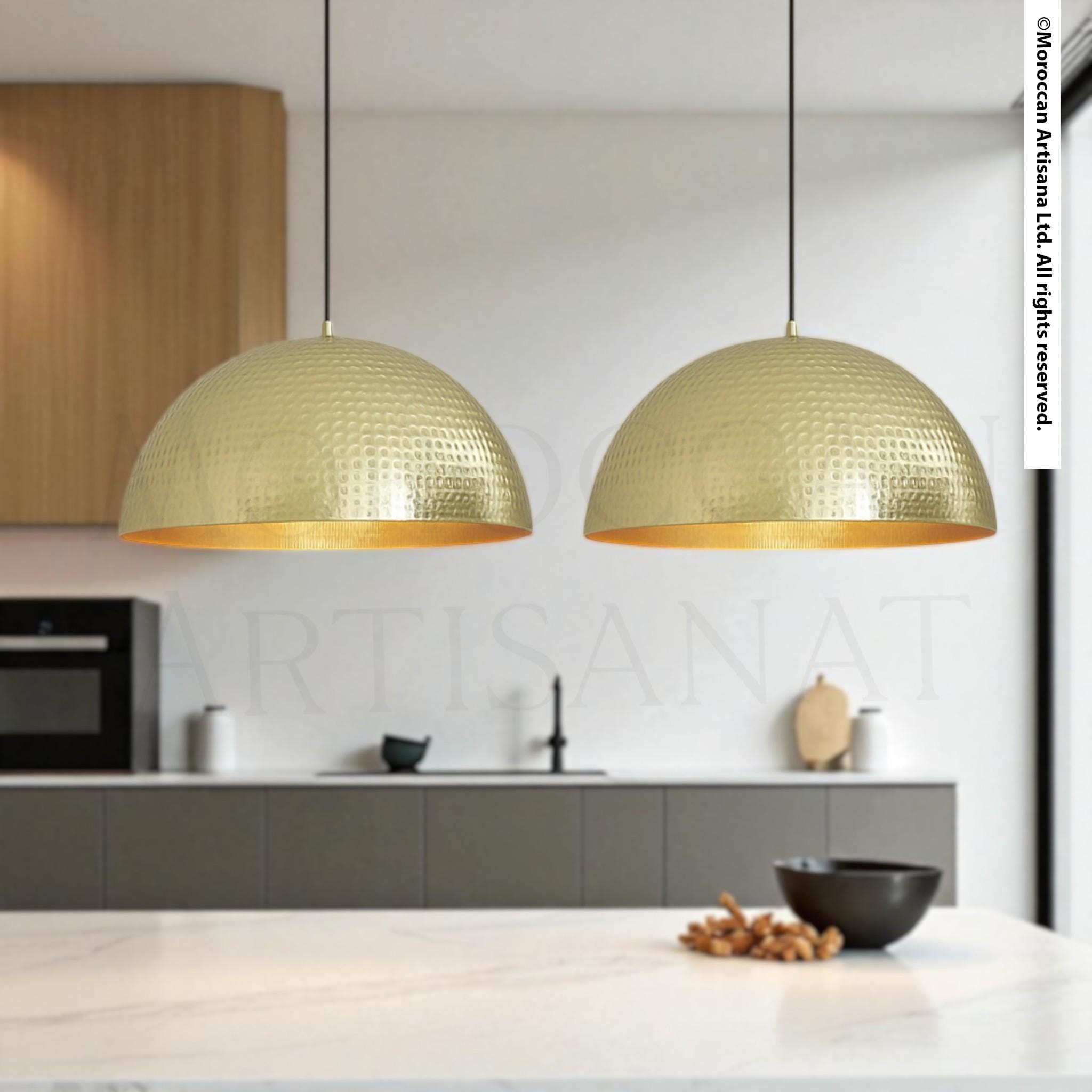 a modern kitchen with two gold-colored pendant lights hanging above a white countertop. The kitchen has a sleek, minimalist design with gray cabinets and a black bowl on the countertop.
