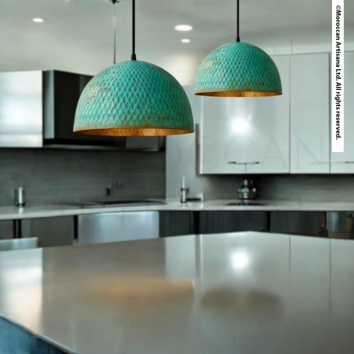 a modern kitchen with a sleek, minimalist design. The focal point is a large, turquoise-colored pendant light hanging above a stainless steel countertop. The countertop has a reflective surface that enhances the overall aesthetic of the space. The kitchen is equipped with stainless steel appliances, including a sink and a refrigerator, which complement the overall design.