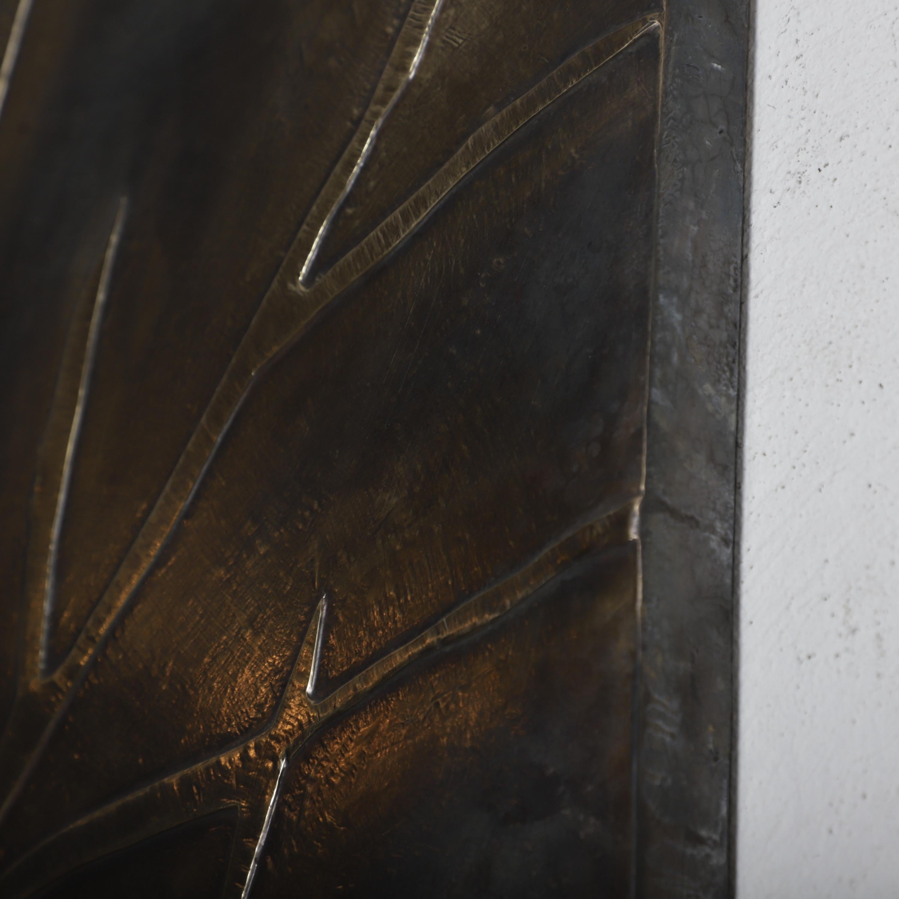 a close-up view of a dark metal surface with a textured, metallic appearance. The surface appears to be made of a shiny, metallic material, possibly bronze or iron. The image does not contain any discernible text or countable objects, and there are no specific actions or movements depicted. The focus is on the surface&#39;s texture and metallic properties.