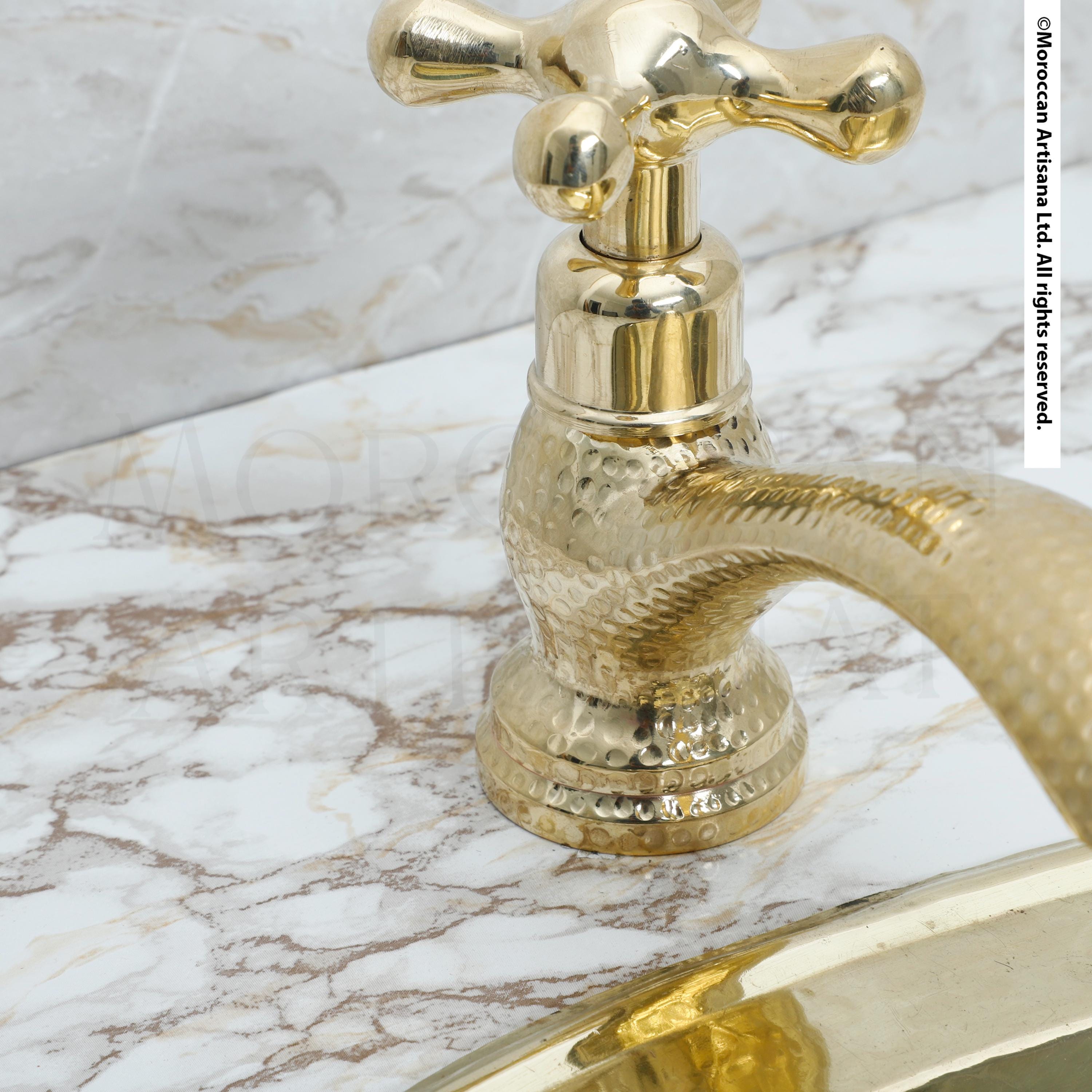 A close-up view of a gold-colored faucet with a textured surface, likely a marble countertop, against a white background.