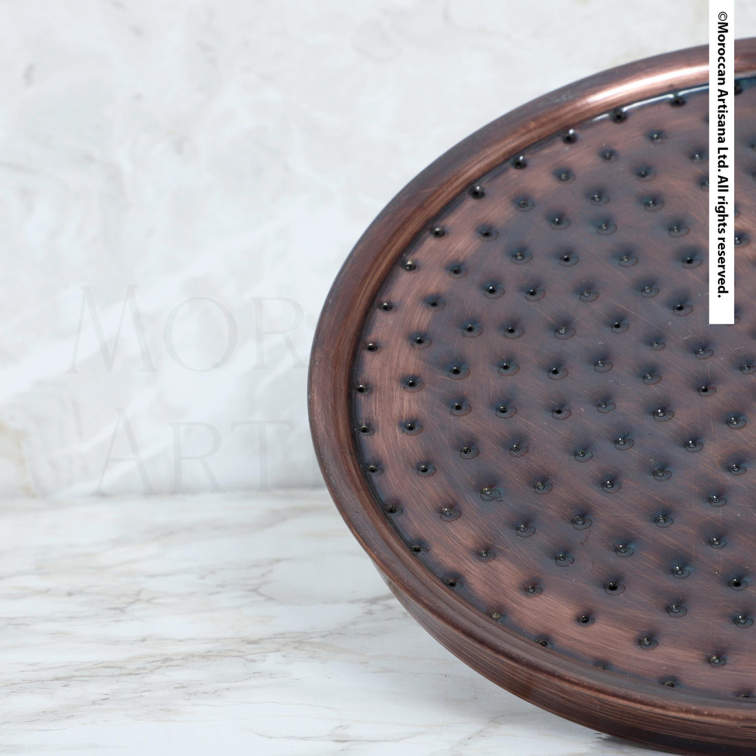 a close-up view of a circular, textured object with a dark brown or bronze color, possibly a piece of metal or a decorative item. The background is a plain white marble surface.