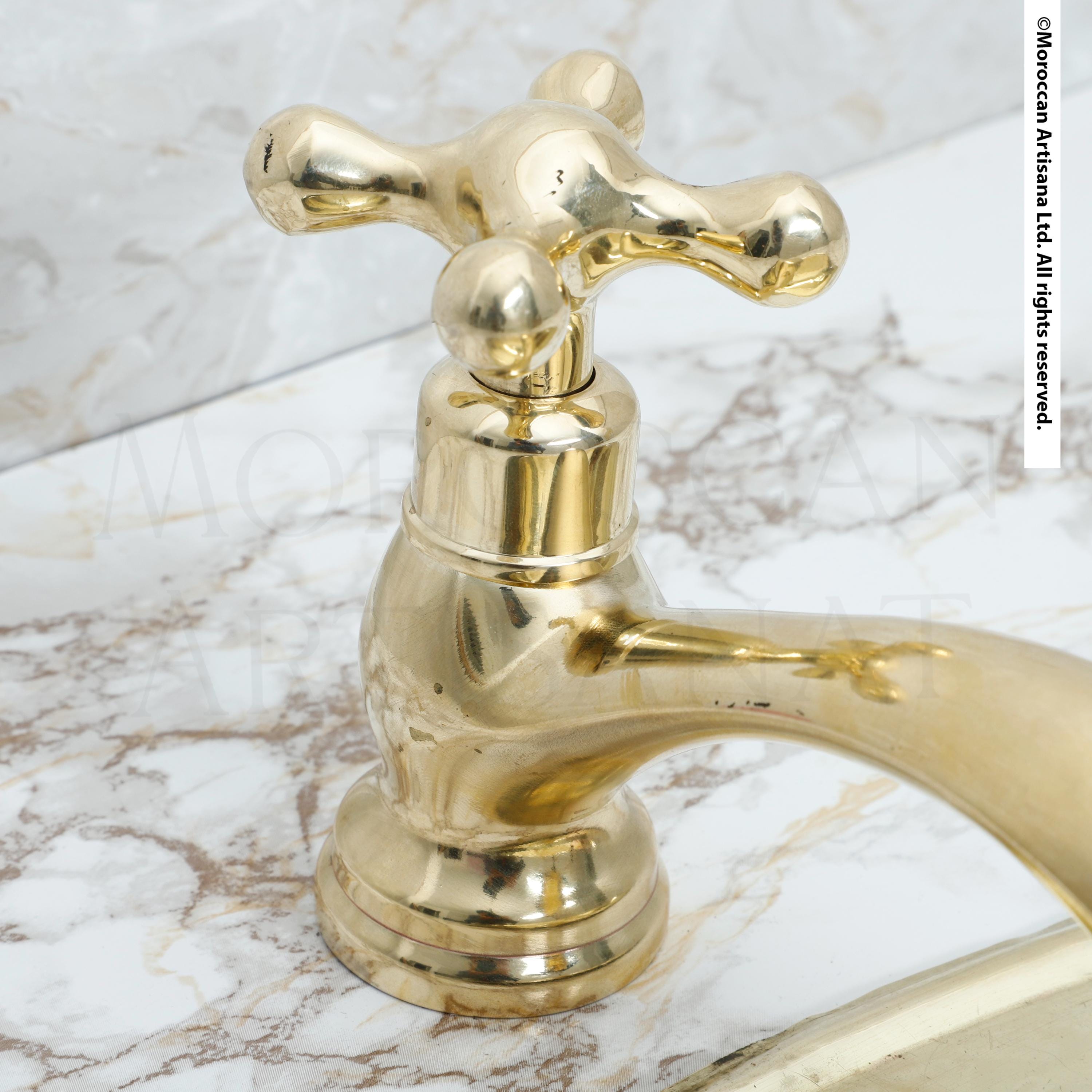 A close-up image of a shiny gold-colored faucet with a curved handle, set against a marble countertop.