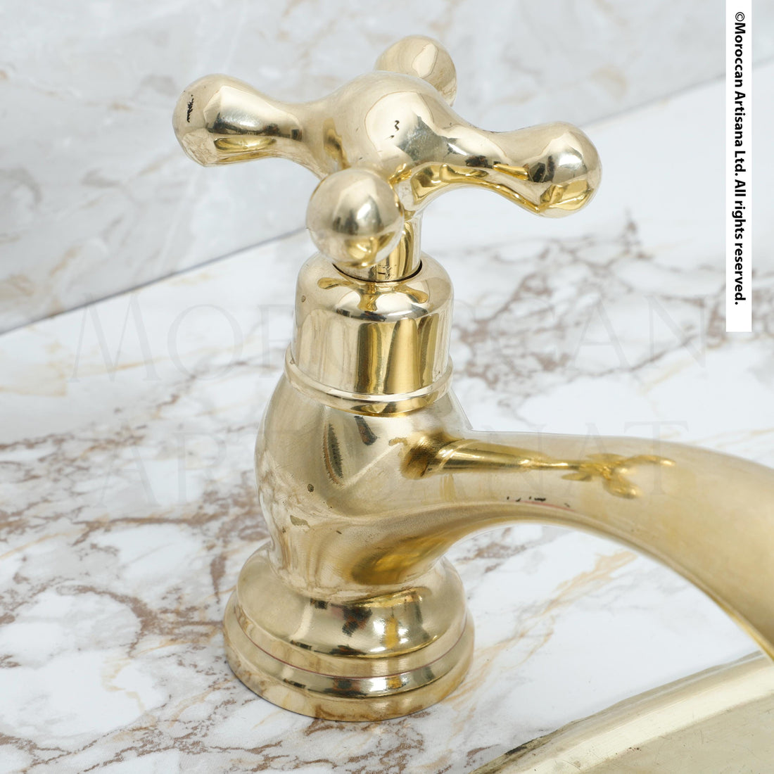 A close-up image of a shiny gold-colored faucet with a curved handle, set against a marble countertop.