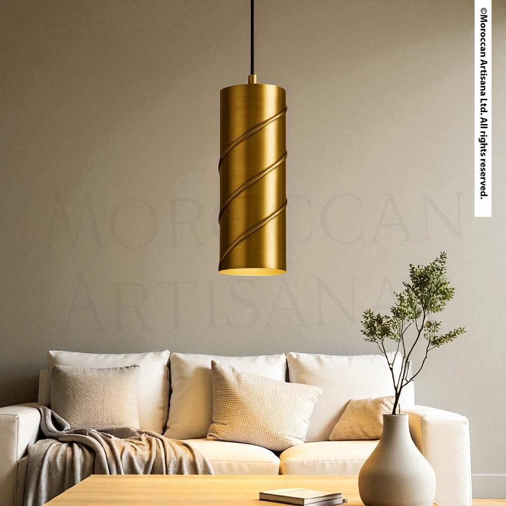 a modern living room with a gold-colored cylindrical pendant light hanging above a white sofa. The sofa is adorned with a plant in a white vase, and there is a wooden coffee table in front of the sofa. The overall color scheme of the room is neutral, with a touch of gold adding a luxurious touch to the space.