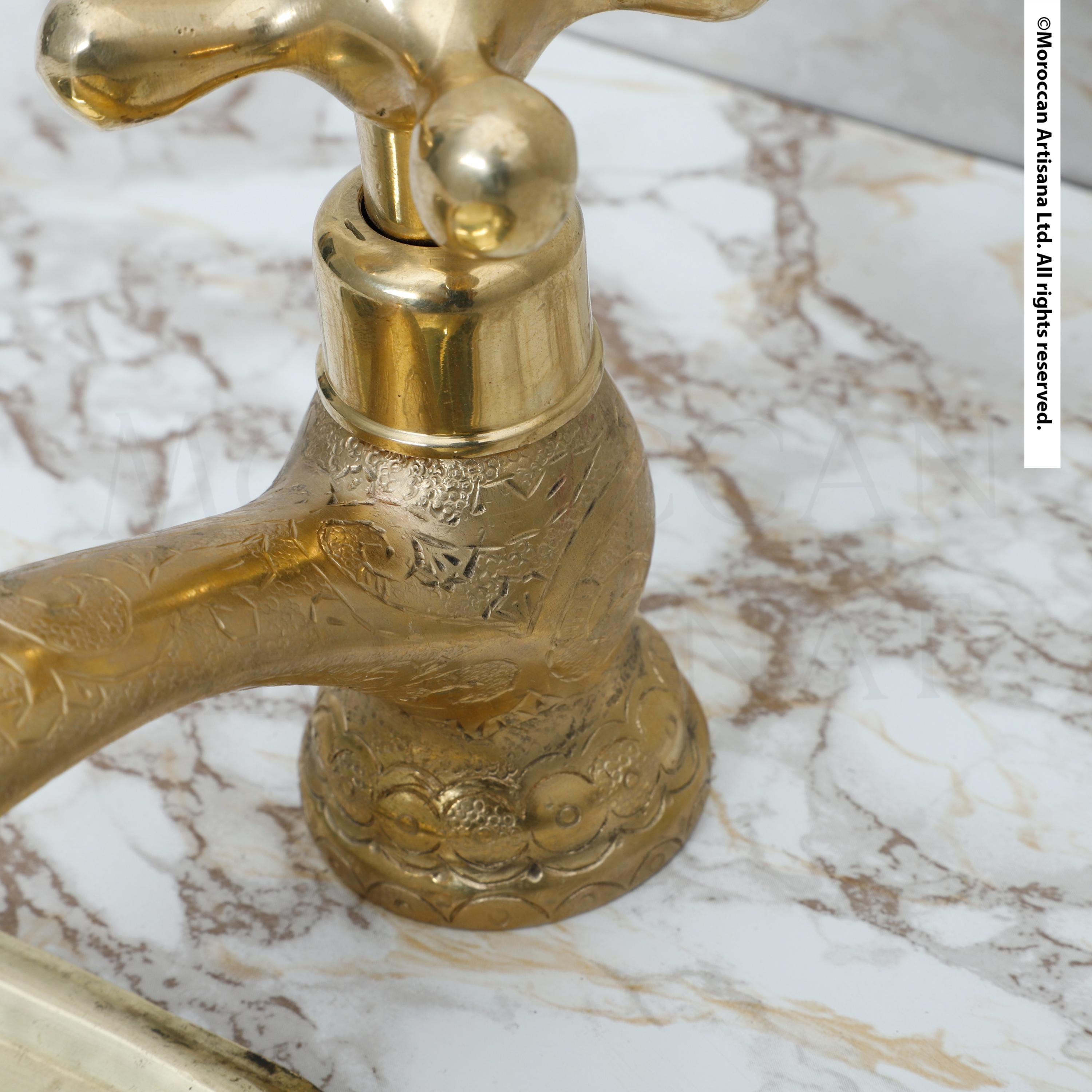 A close-up view of a decorative brass faucet with intricate patterns on its surface, set against a marble countertop.