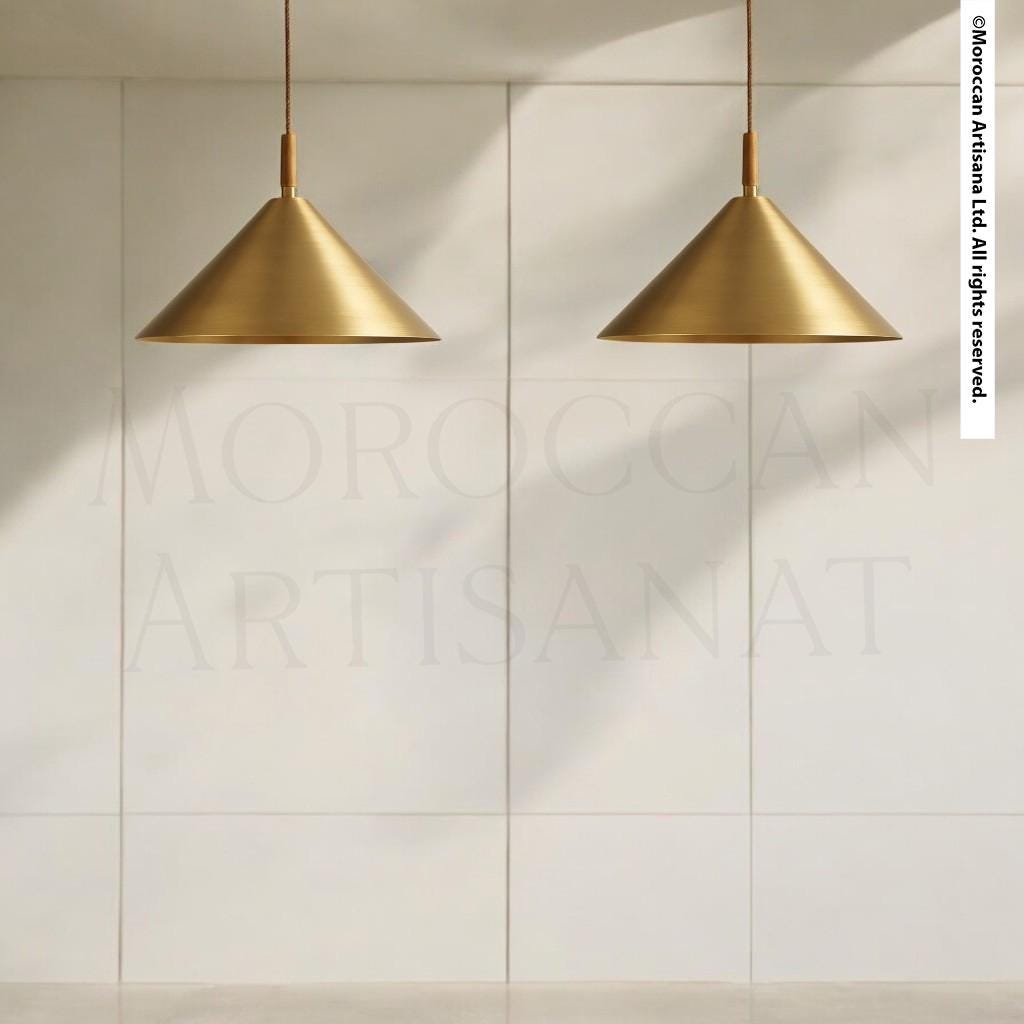 two gold pendant lights hanging from the ceiling, casting a shadow on the white wall behind them.