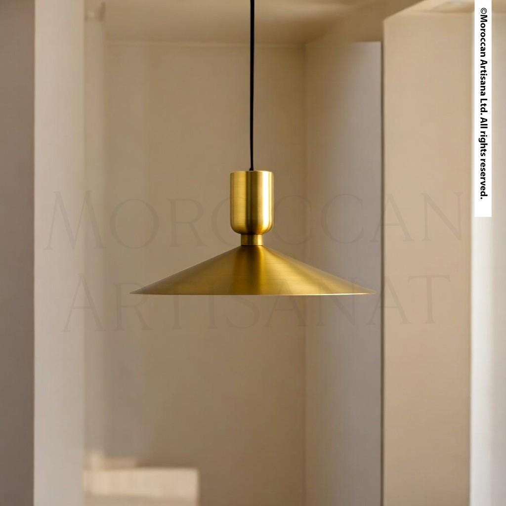A gold-colored pendant light hangs from the ceiling in a room with a white wall and a window.