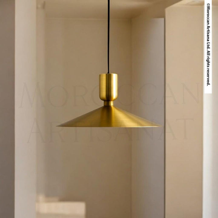 A gold-colored pendant light hangs from the ceiling in a room with a white wall and a window.