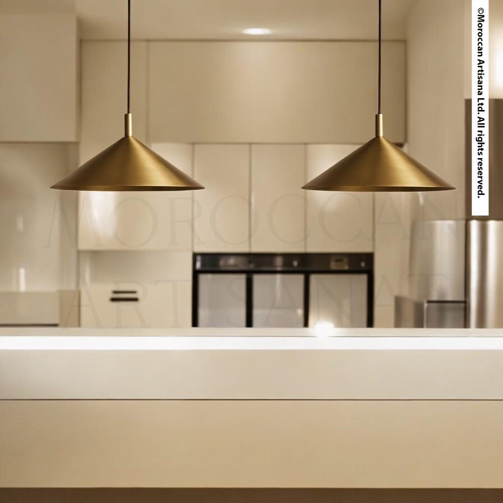 a modern kitchen with a sleek, minimalist design. The kitchen is equipped with stainless steel appliances, including a refrigerator and an oven, and has a clean, white countertop. Two pendant lights hang above the countertop, providing illumination to the space. The overall aesthetic of the kitchen is contemporary and sophisticated, with a focus on functionality and simplicity.