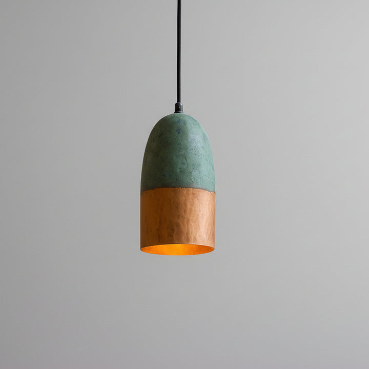 A modern pendant light with a green and orange color scheme hangs from the ceiling against a textured beige wall.