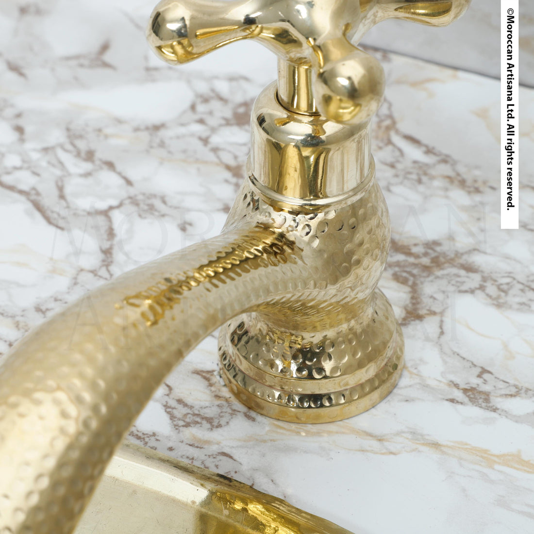 A close-up view of a shiny, golden-colored faucet with a textured, metallic finish, set against a marble countertop.