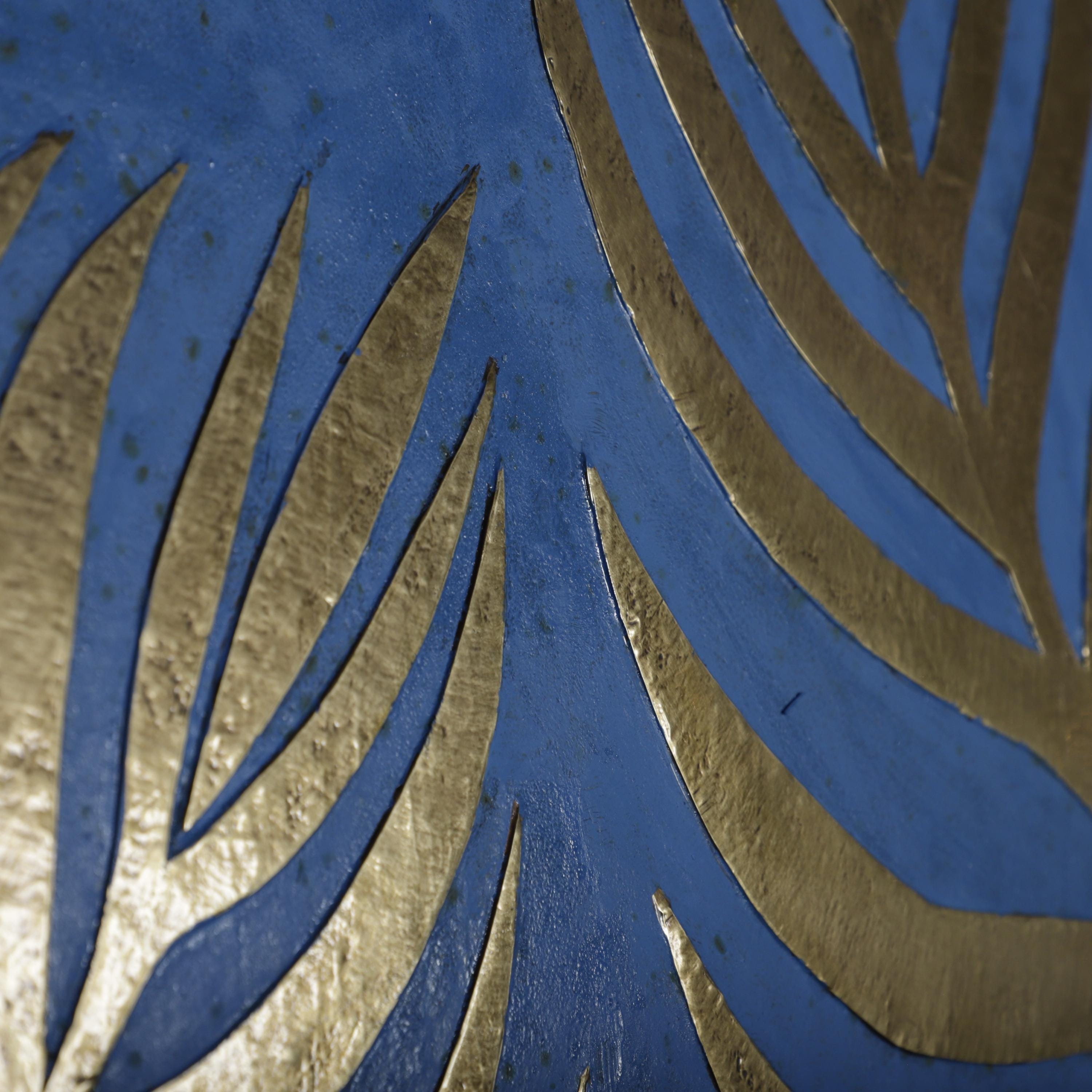 a close-up view of a blue surface with gold leaf-like patterns. The patterns are composed of overlapping curved lines, creating a visually striking and intricate design.