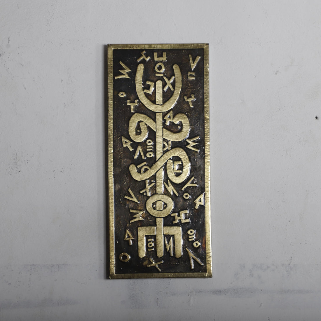 a rectangular metal plaque with an intricate design and various symbols and characters on it.