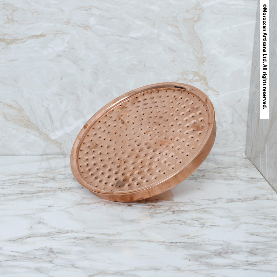 A copper-colored shower head with a perforated surface is shown against a marble background.