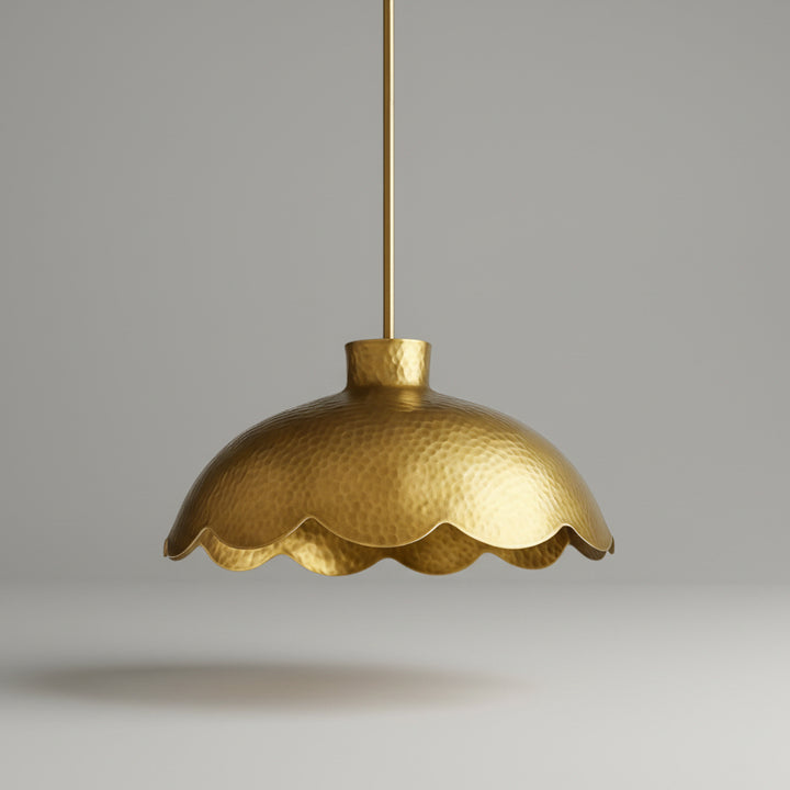 A gold-colored pendant light fixture with a scalloped edge hangs from a hook against a beige background.