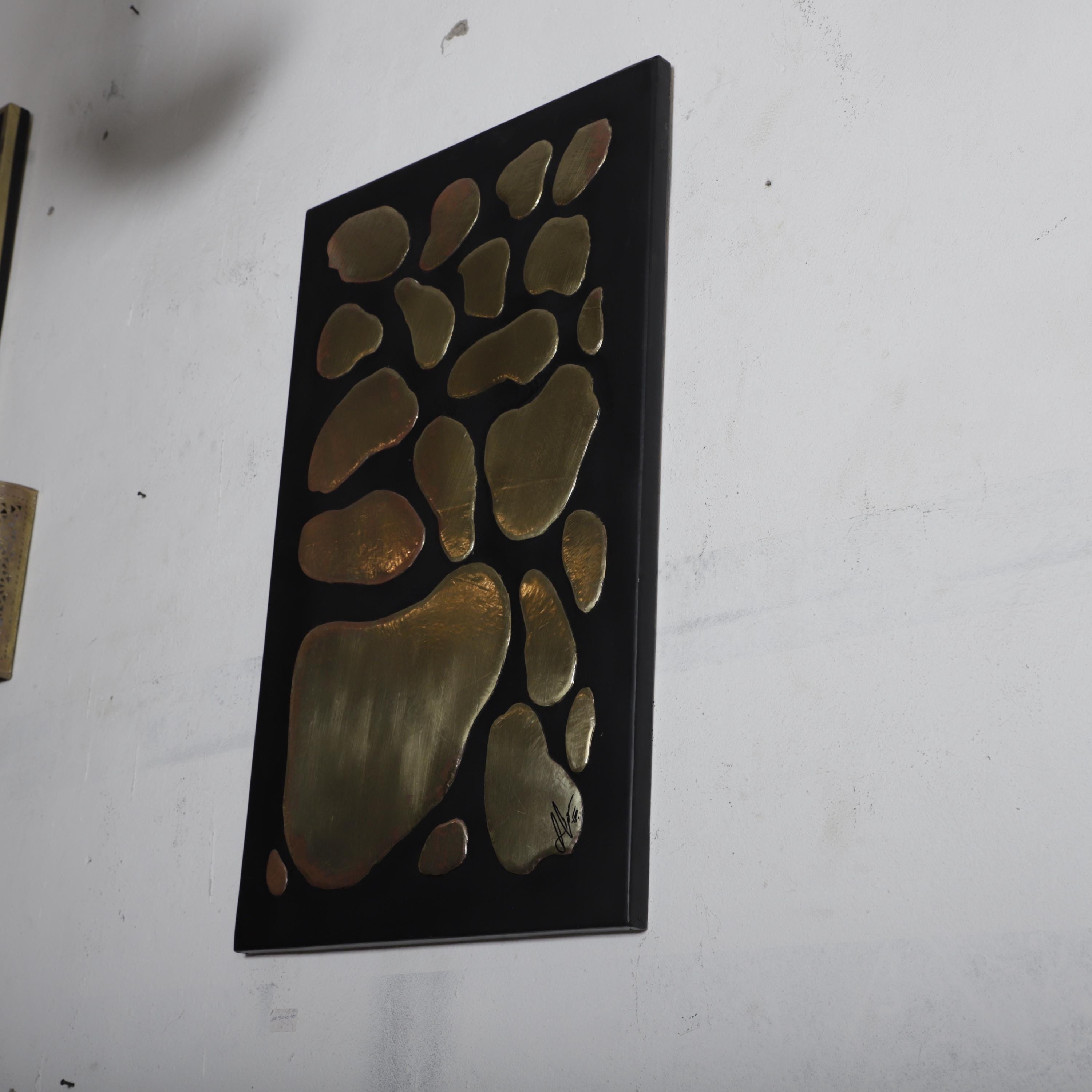 a black frame with a gold-colored abstract design on it, hanging on a white wall.