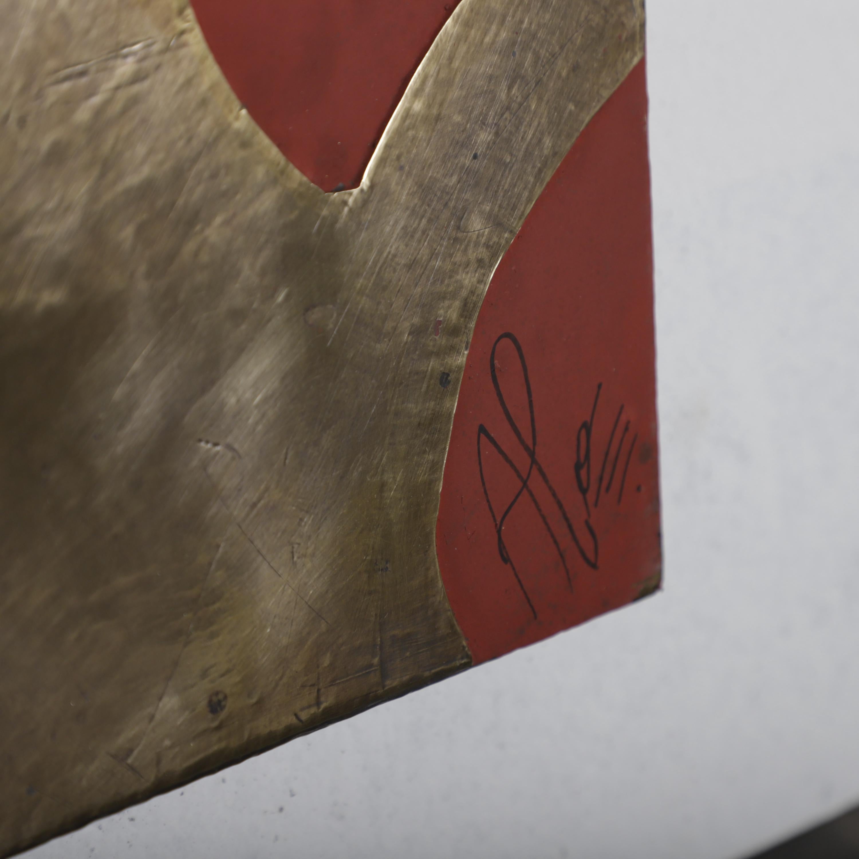 a close-up view of a metallic surface with a red and gold pattern. There is a signature or autograph in the bottom right corner of the image.