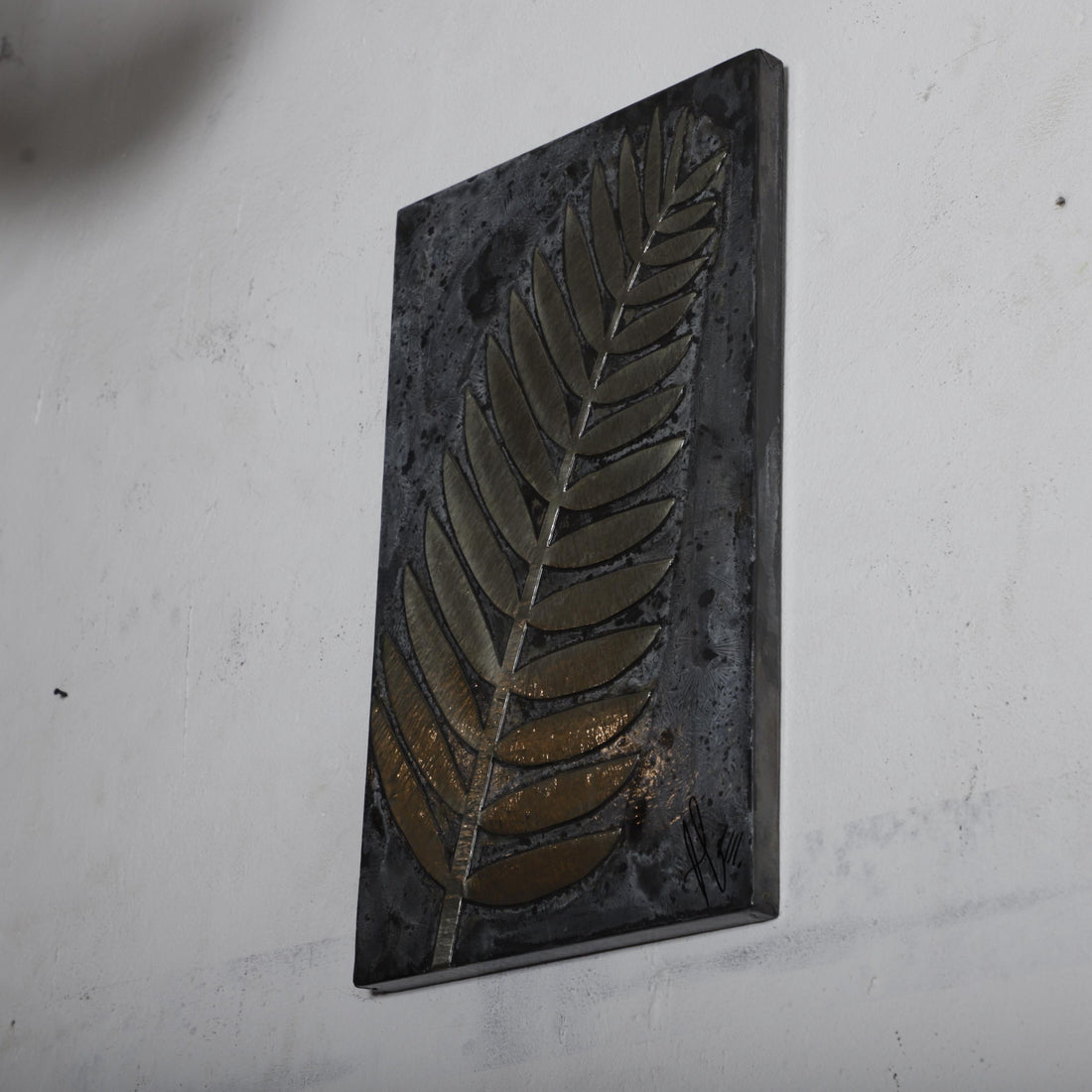 a black rectangular artwork with a leaf-like design on it, mounted on a white wall.