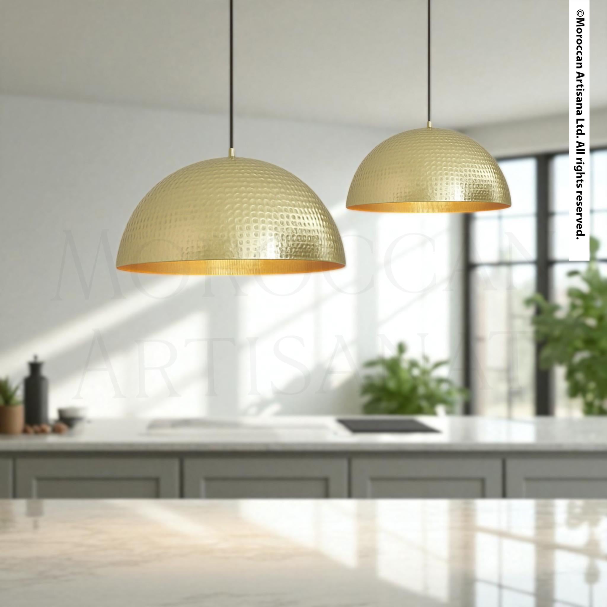 two gold-colored pendant lights hanging from the ceiling in a modern kitchen setting.