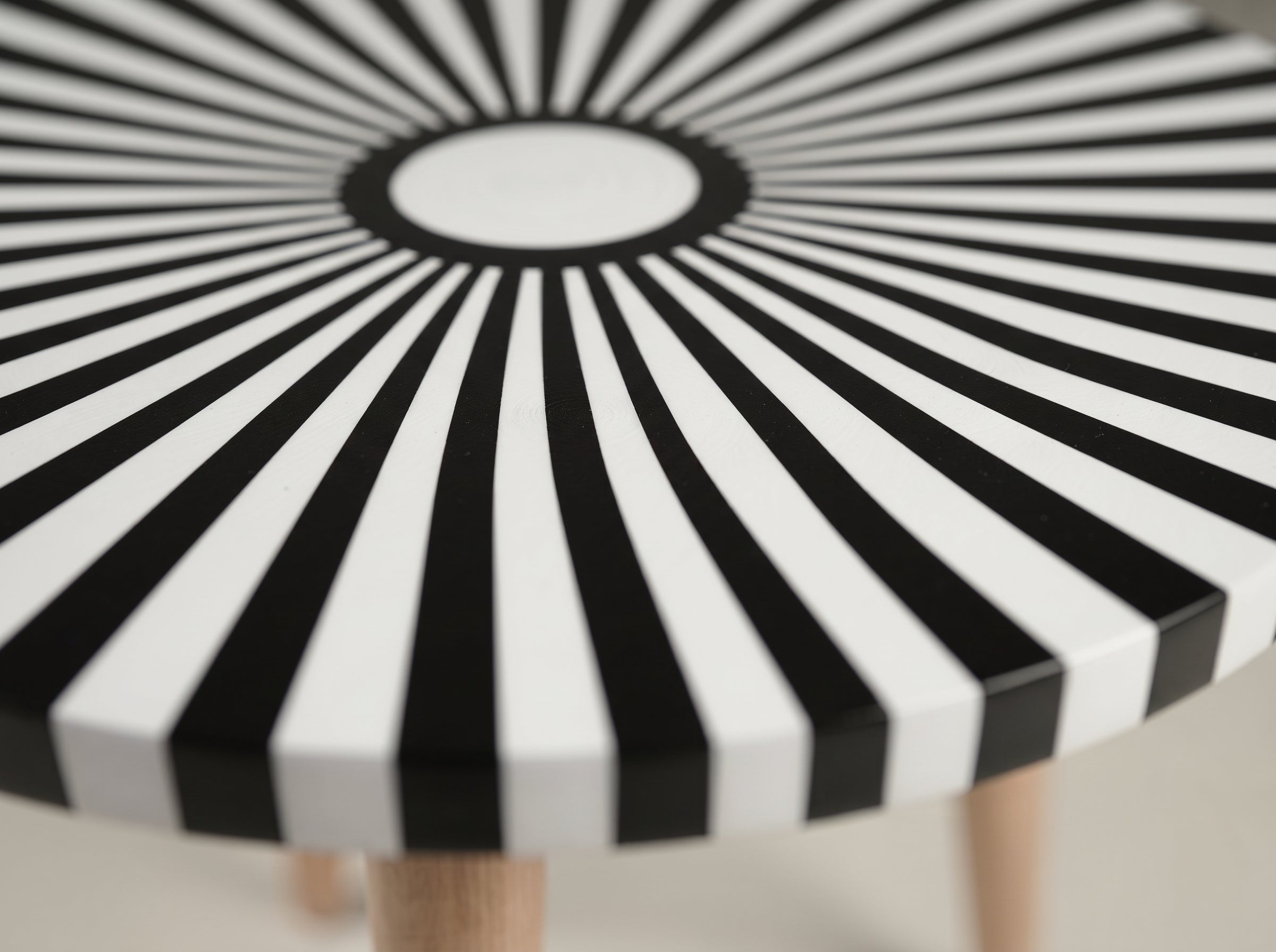 A close-up of a round table with a bold black and white sunburst pattern on the tabletop and light wood legs.