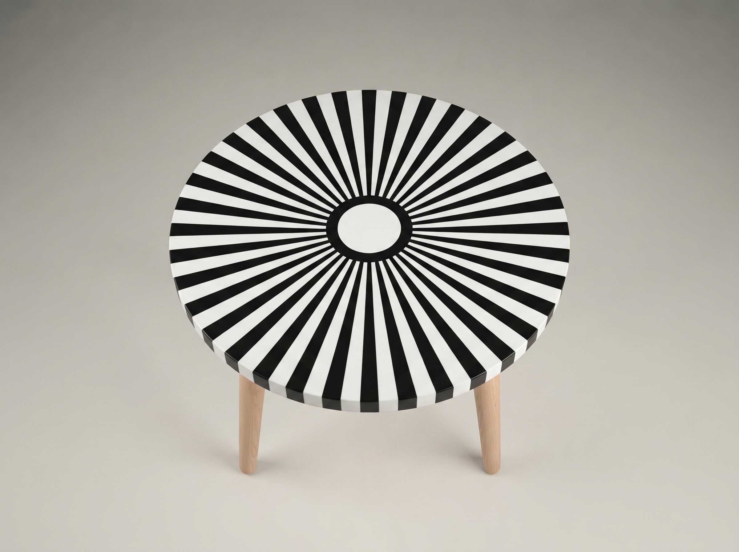 A round accent table with a black and white radial striped pattern on the top and three light wood legs, shown against a neutral gray background.